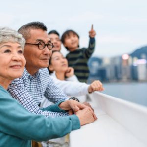 Relaxed senior Chinese woman and husband enjoying Hong Kong views with extended family at Ocean Terminal Deck atop Harbour City Shopping Centre.